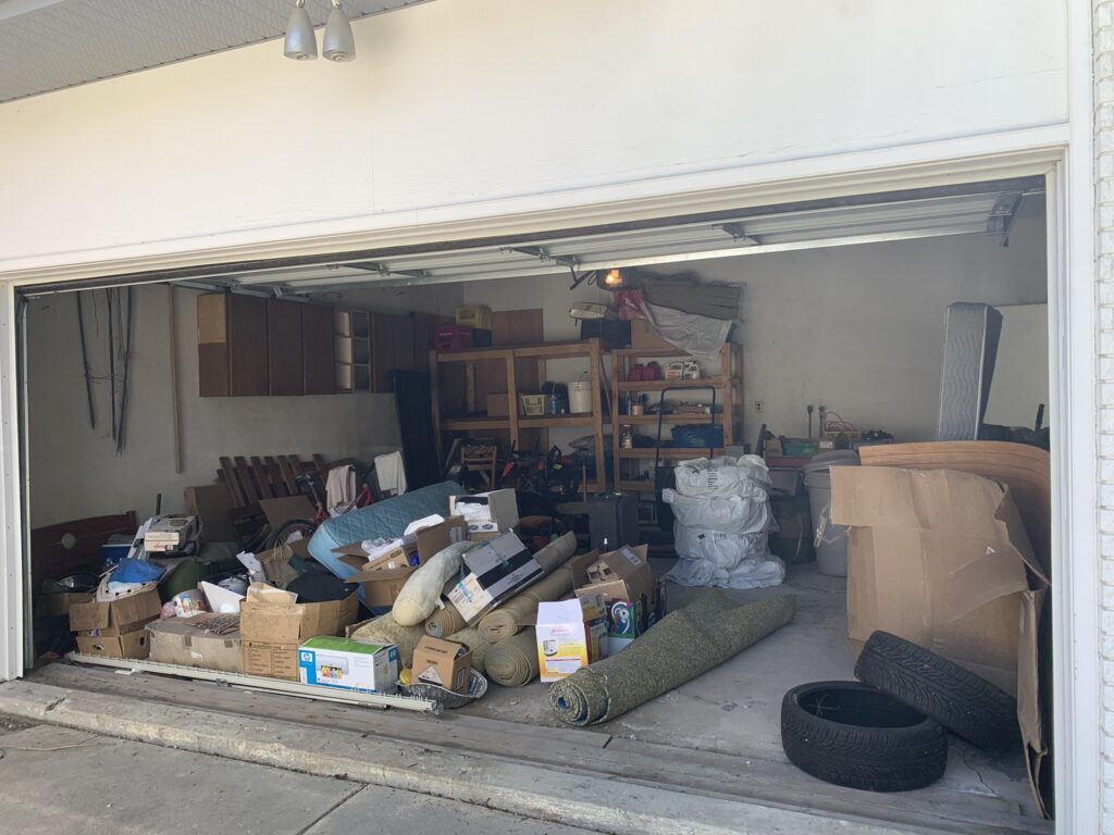 A garage that is littered with objects such as carpet, paint cans, and boxes